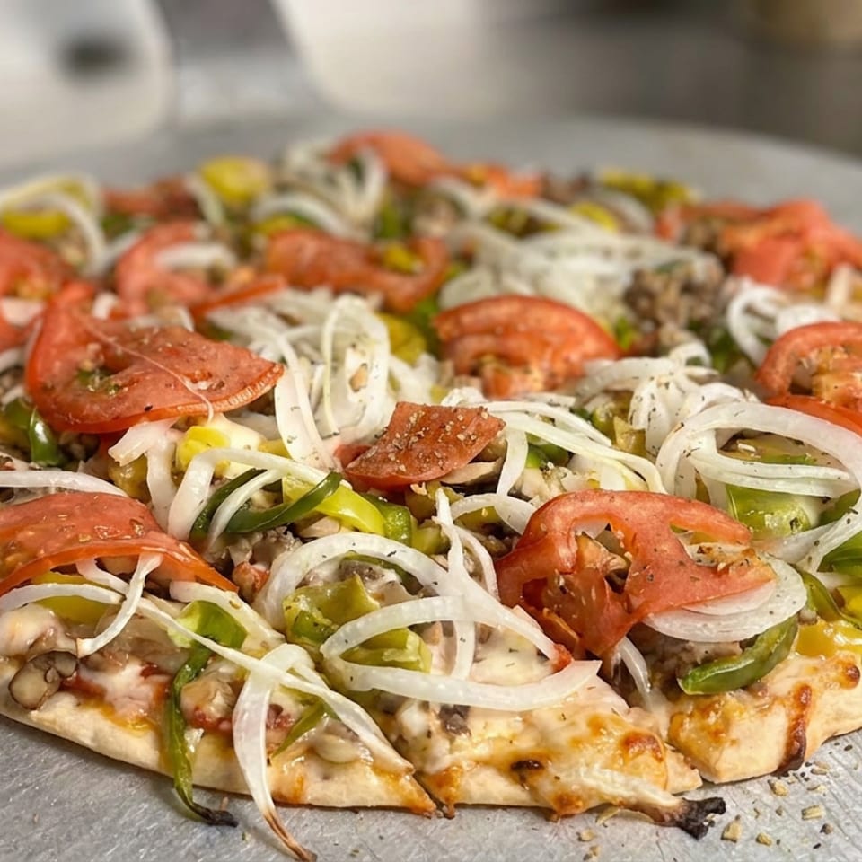 Loaded pizza topped with sliced tomatoes, onions, green peppers, mushrooms, and pepperoni on a metal serving tray.